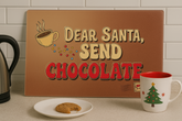 Decorative sign with 'Dear Santa, Send Chocolate' text on a kitchen counter with a mug and cookies.