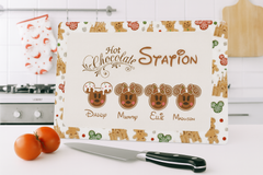 Glass cutting board with gingerbread design and 'Hot Chocolate Station' text on a kitchen counter.